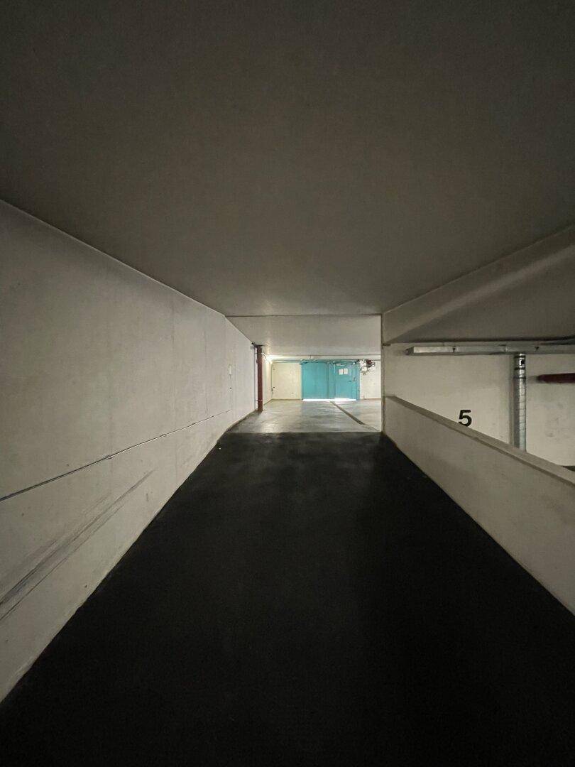 Einfahrt zur Tiefgarage mit einer Rampe, Betonwänden und dunklem Bodenbelag, der in die Tiefe führt.