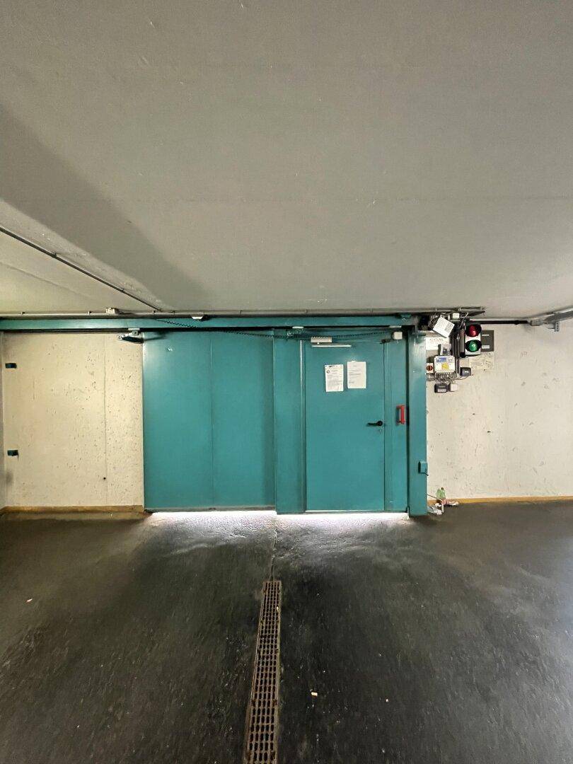Große türkisfarbene Metalltür in der Tiefgarage, ausgestattet mit einem Ampelsystem und Hinweisschildern.