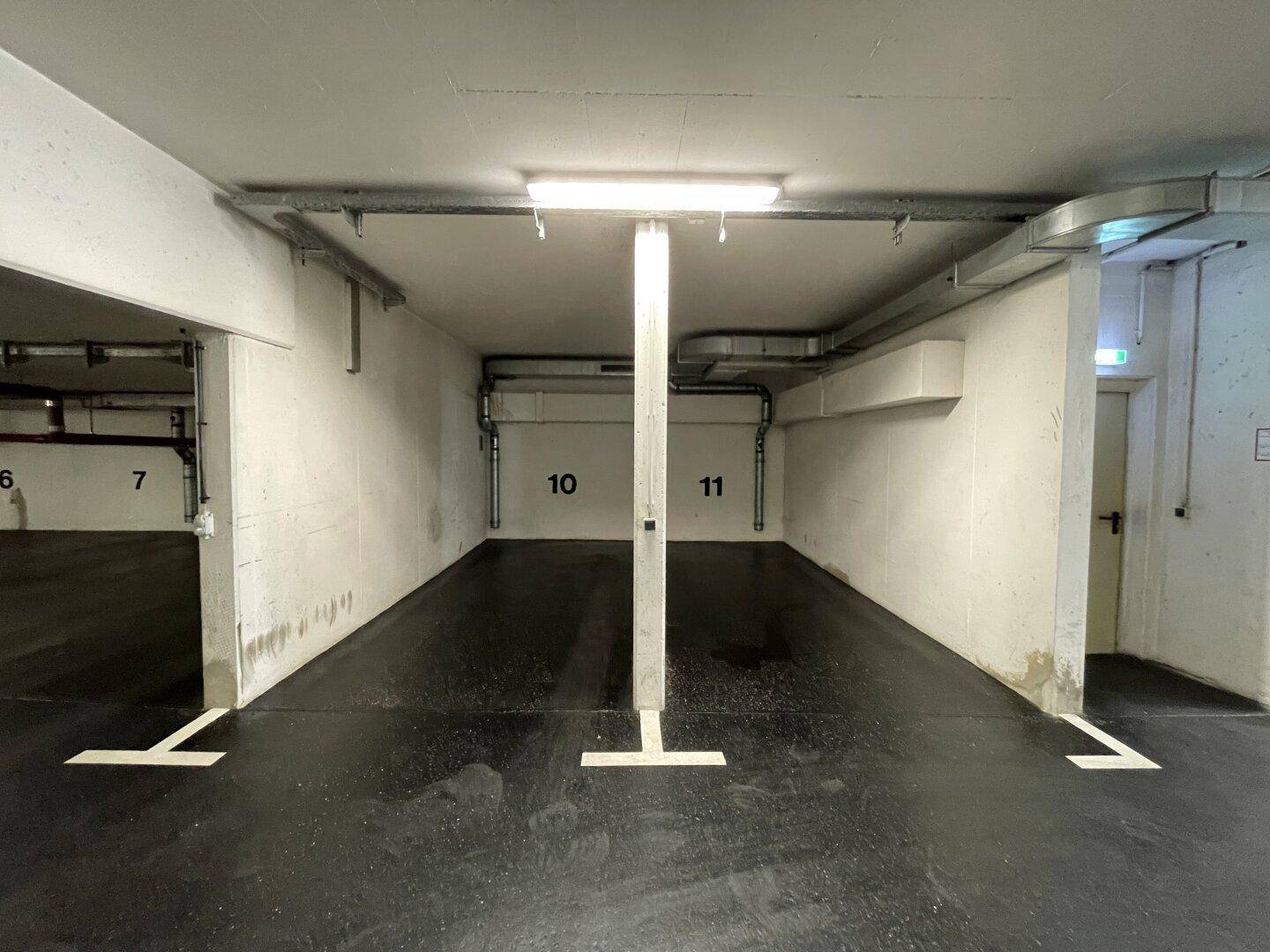 Zwei nummerierte Stellplätze in einer Tiefgarage mit Betonpfeilern und Deckenbeleuchtung, bereit zur Nutzung.