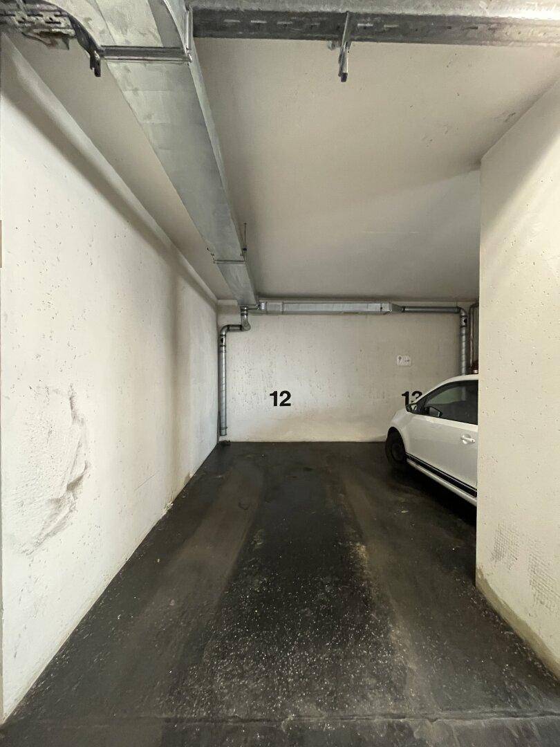 Einzelner Stellplatz Nummer 12 in einer Tiefgarage, teilweise von einem geparkten weißen Auto belegt.