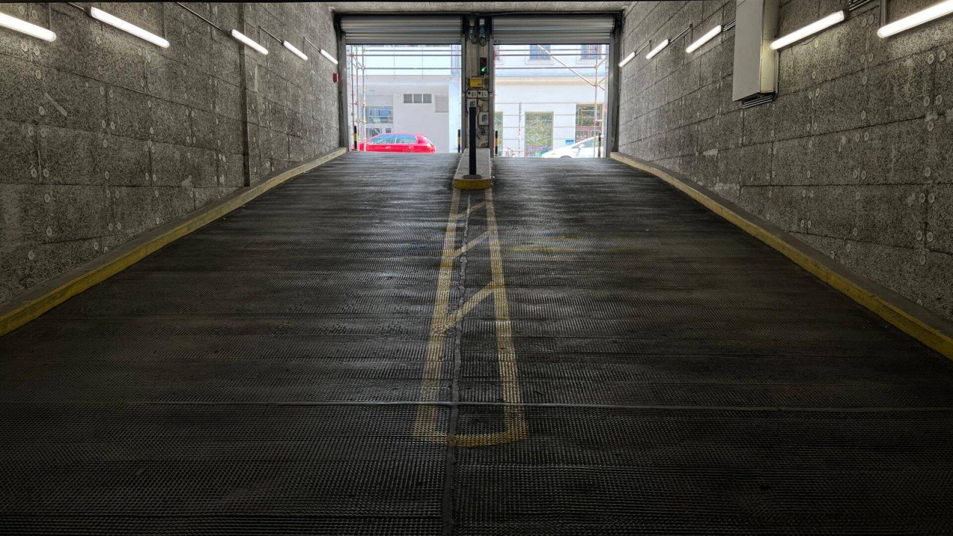 Ausfahrt einer Tiefgarage mit einer Rampe, grauen Betonwänden und Tageslicht am Ende des Tunnels.