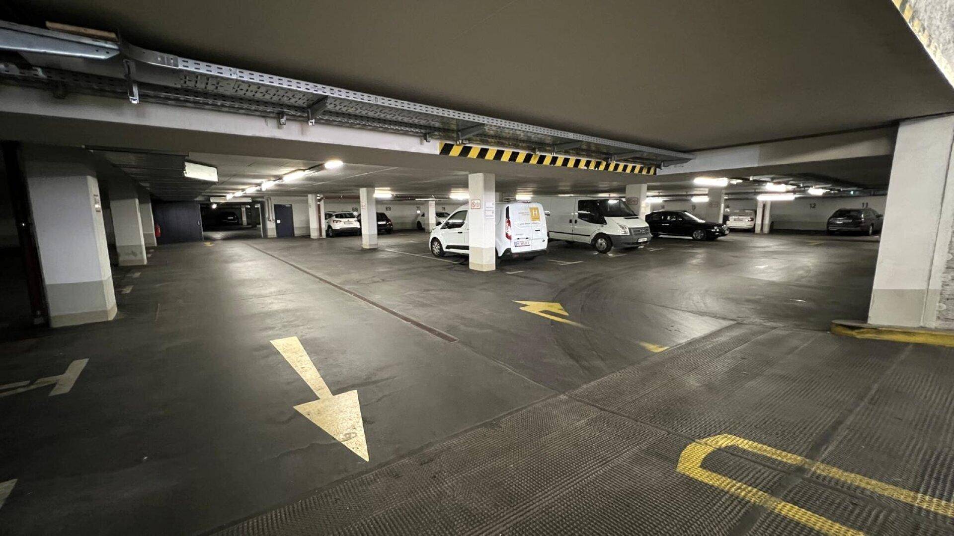 Geräumige Tiefgarage mit zahlreichen Stellplätzen, Säulen und Deckenbeleuchtung, gut beleuchtet und sauber.
