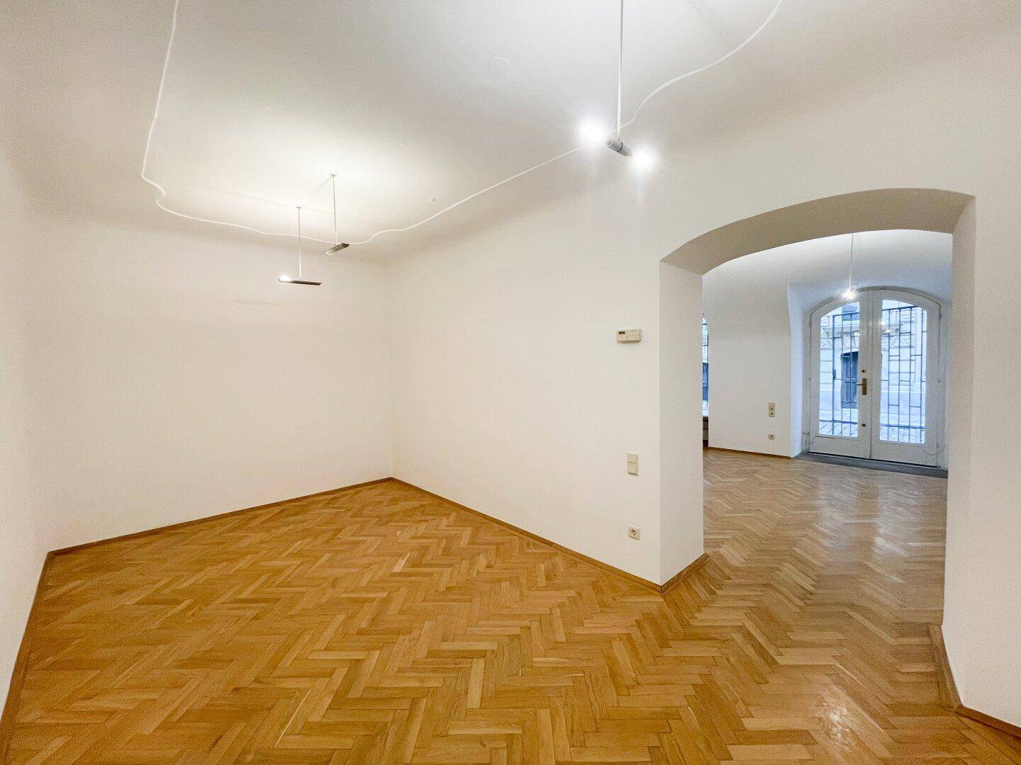 Offener Wohnbereich mit Fischgrätparkett, einem Rundbogen und Blick auf die großen Eingangstüren.