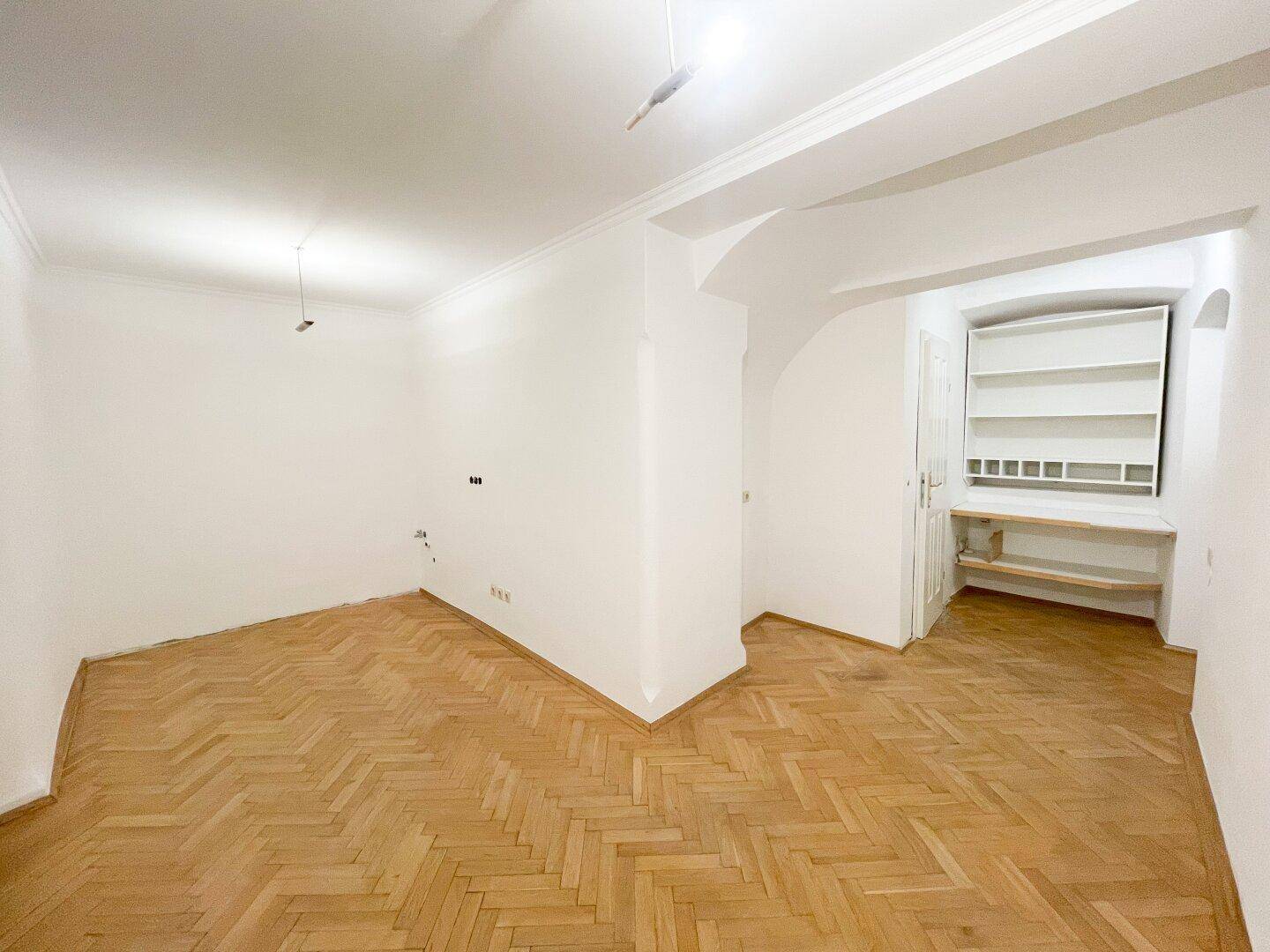 Heller Raum mit Fischgrätparkett und einer praktischen Einbauregalwand in einer Nische.
