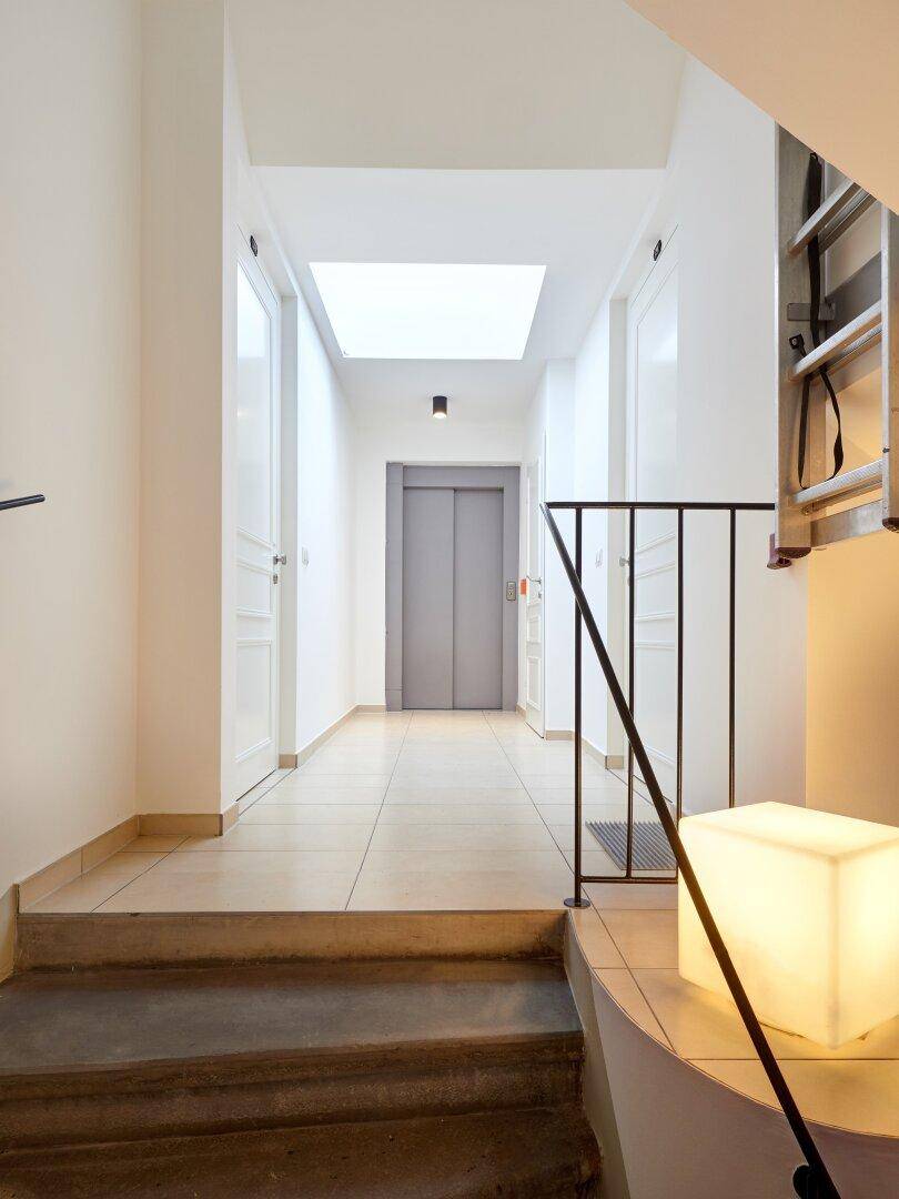 Heller Treppenaufgang mit Fliesenboden, modernem Licht und Zugang zum Aufzug.