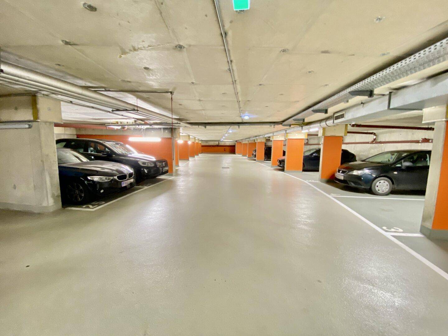Geräumige Tiefgarage mit markierten Parkplätzen und orangefarbenen Säulen, einige Fahrzeuge sind bereits geparkt.