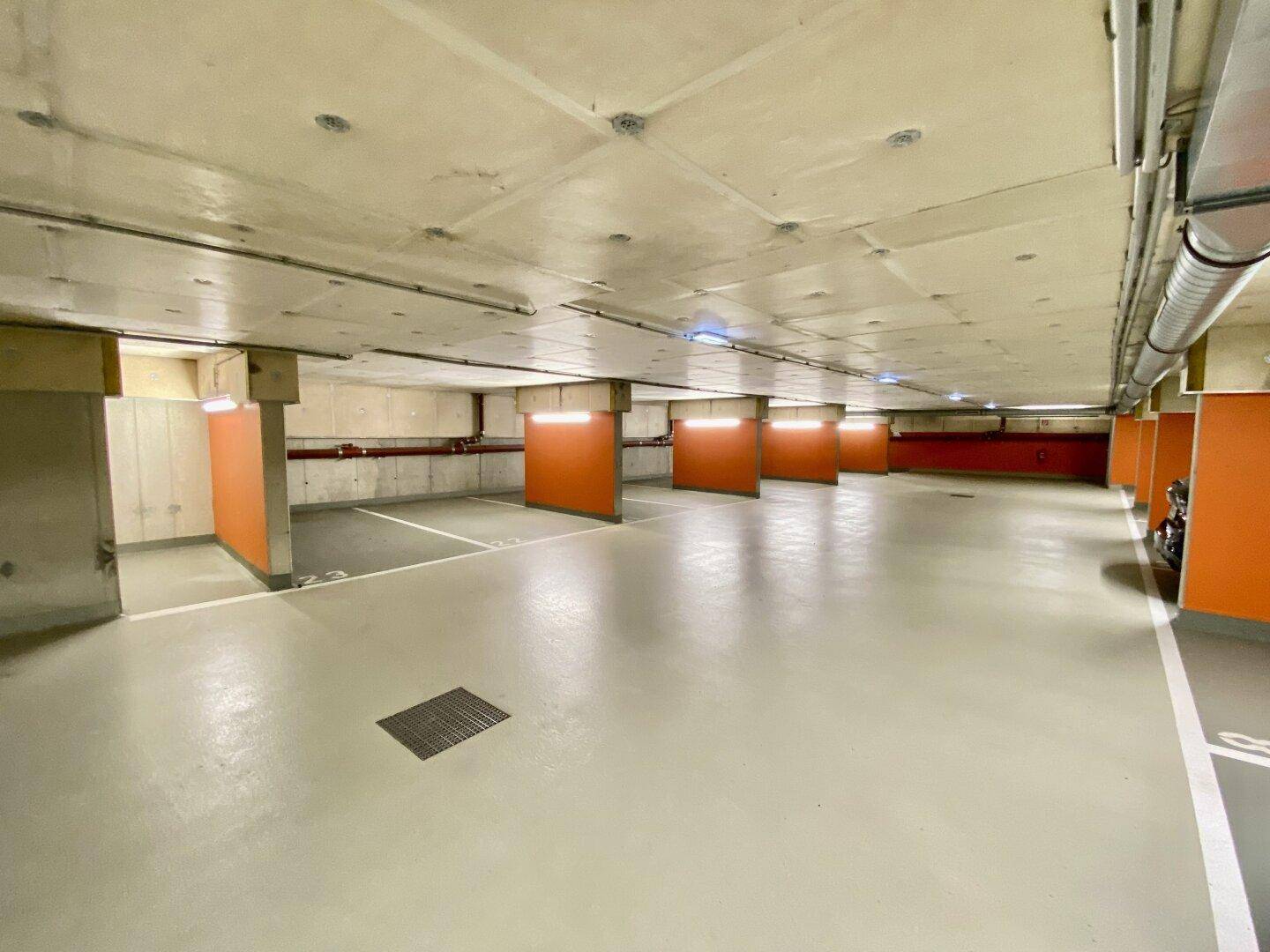 Leerer Bereich einer Tiefgarage mit sauber markierten Parkplätzen und orangefarbenen Akzenten an den Säulen.