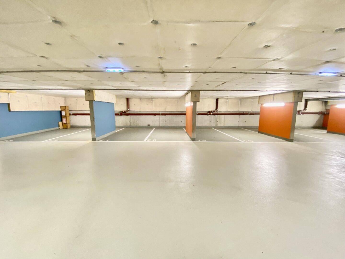 Weitläufige Tiefgarage mit einer Mischung aus orangefarbenen und blauen Säulen und vielen freien Stellplätzen.