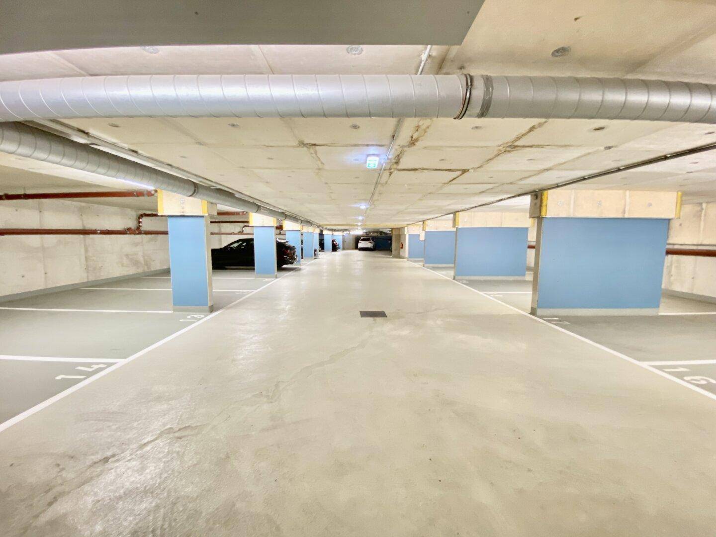 Lange Reihe von Parkplätzen in einer Tiefgarage mit blauen Säulen und Decken aus Sichtbeton.