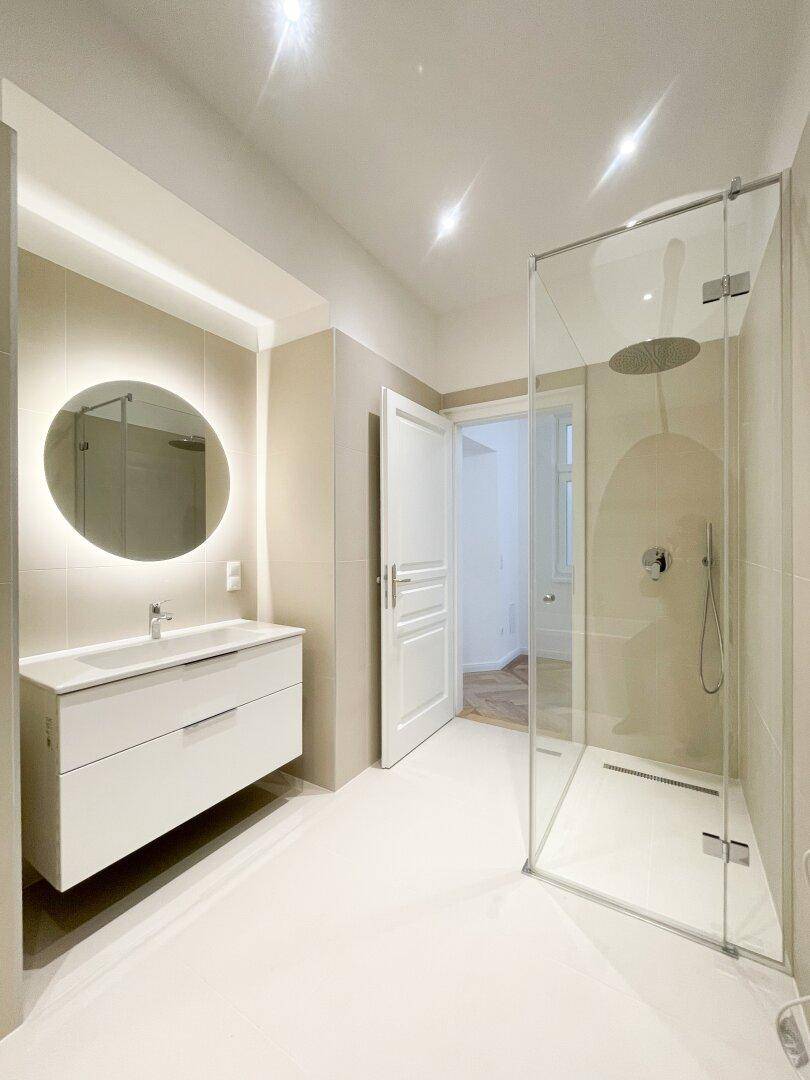 Elegantes Badezimmer mit moderner begehbarer Dusche, Einzelwaschbecken und beleuchtetem Spiegel.