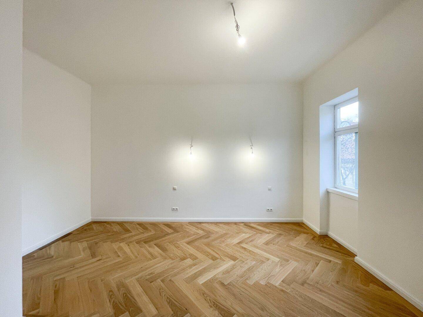 Ruhiges Zimmer mit Fischgrätparkett und einem Fenster, ideal als Schlafzimmer oder Arbeitszimmer.