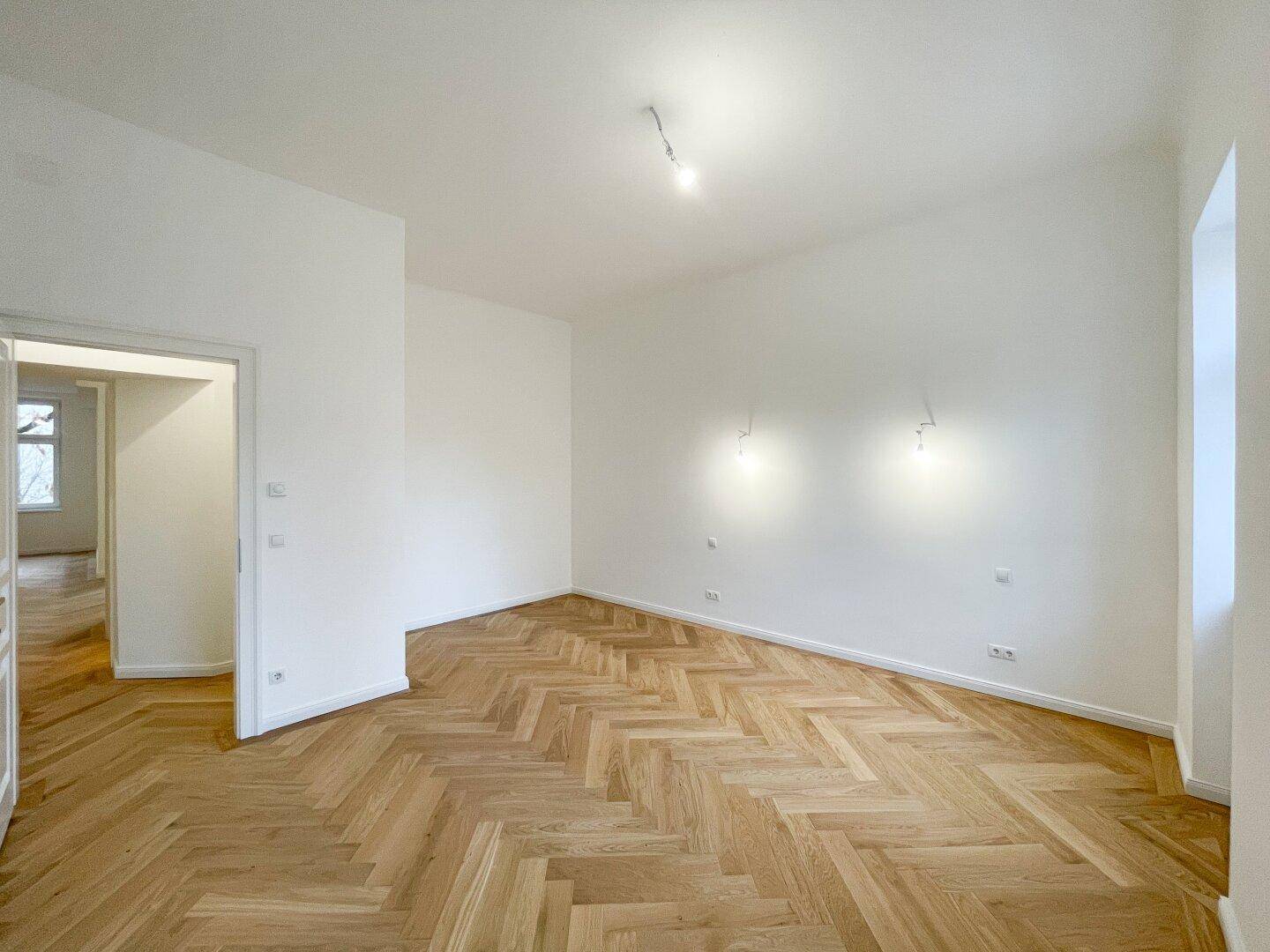 Geräumiges Zimmer mit Fischgrätparkett und weiß gestrichenen Wänden, ideal für ein Schlafzimmer.