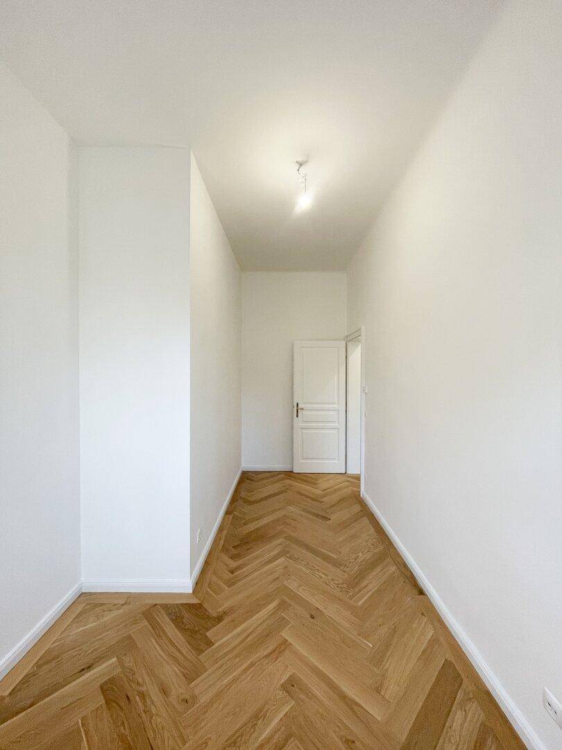 Heller Flur mit Fischgrätparkett und einer Tür am Ende, die zu weiteren Räumen führt.