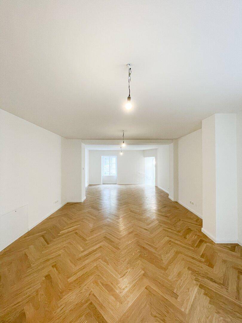 Weitläufiger Wohnbereich mit glänzendem Fischgrätparkett und hohen Decken, ideal für offene Wohnkonzepte.