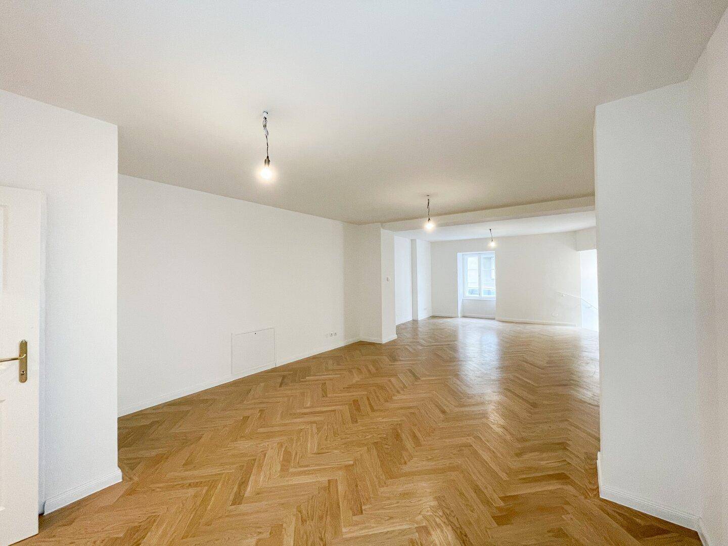 Geräumiges, leeres Wohnzimmer mit Fischgrätparkett und weißen Wänden, bereit zur individuellen Gestaltung.