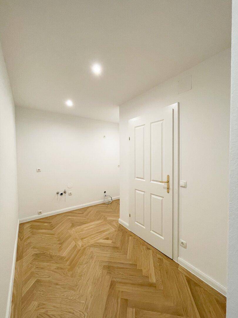 Heller Flur mit Fischgrätparkett und vorbereiteten Anschlüssen, ideal für eine kleine Küche oder Waschküche.