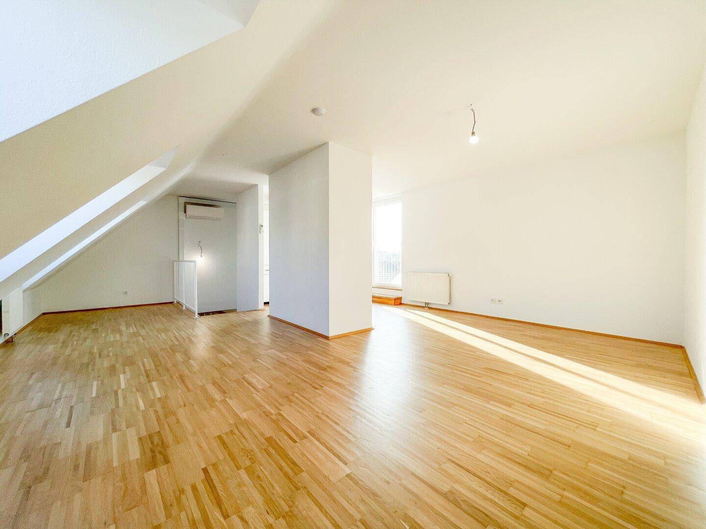 Helles und geräumiges Dachgeschosszimmer mit Holzboden und schrägen Wänden, ideal für ein Wohnzimmer.