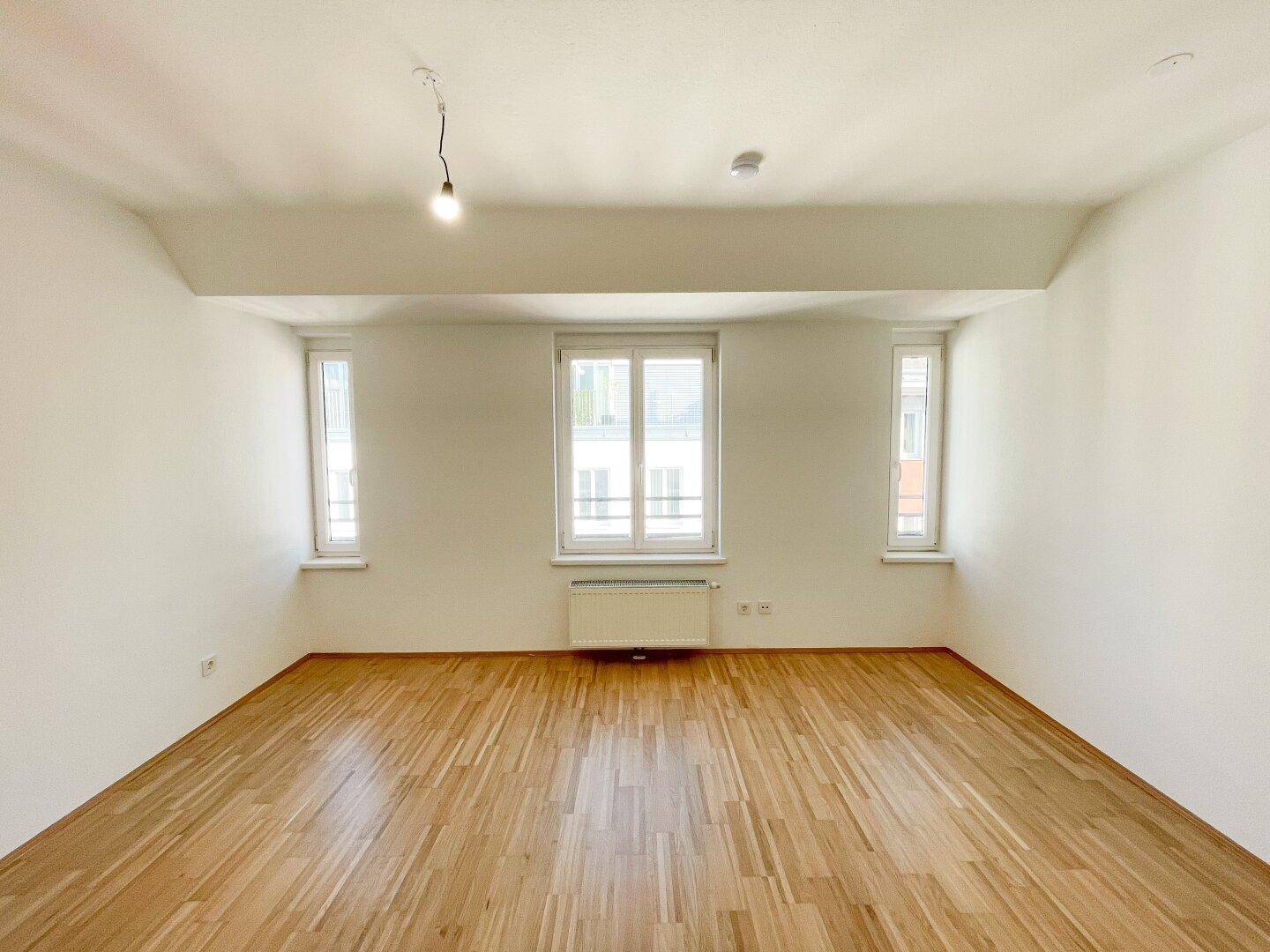 Geräumiges Zimmer mit Holzboden und großen Fenstern, bietet viel Tageslicht und eine angenehme Atmosphäre.