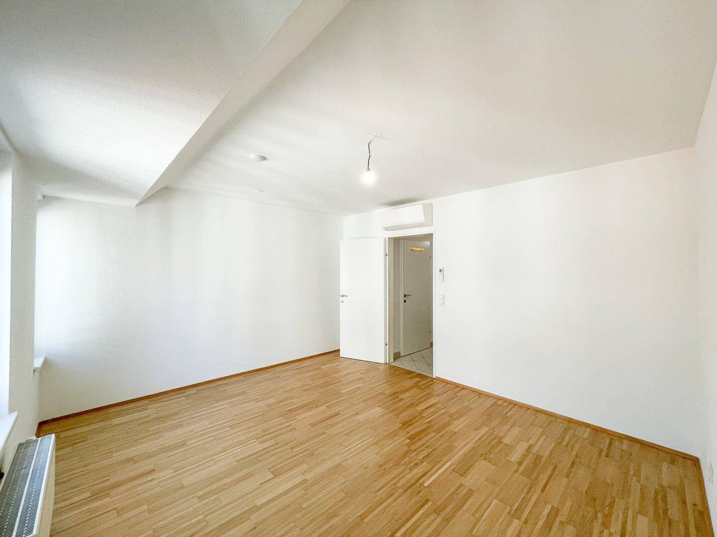 Heller Raum mit Holzboden und Klimaanlage, ideal als Schlaf- oder Wohnzimmer nutzbar.