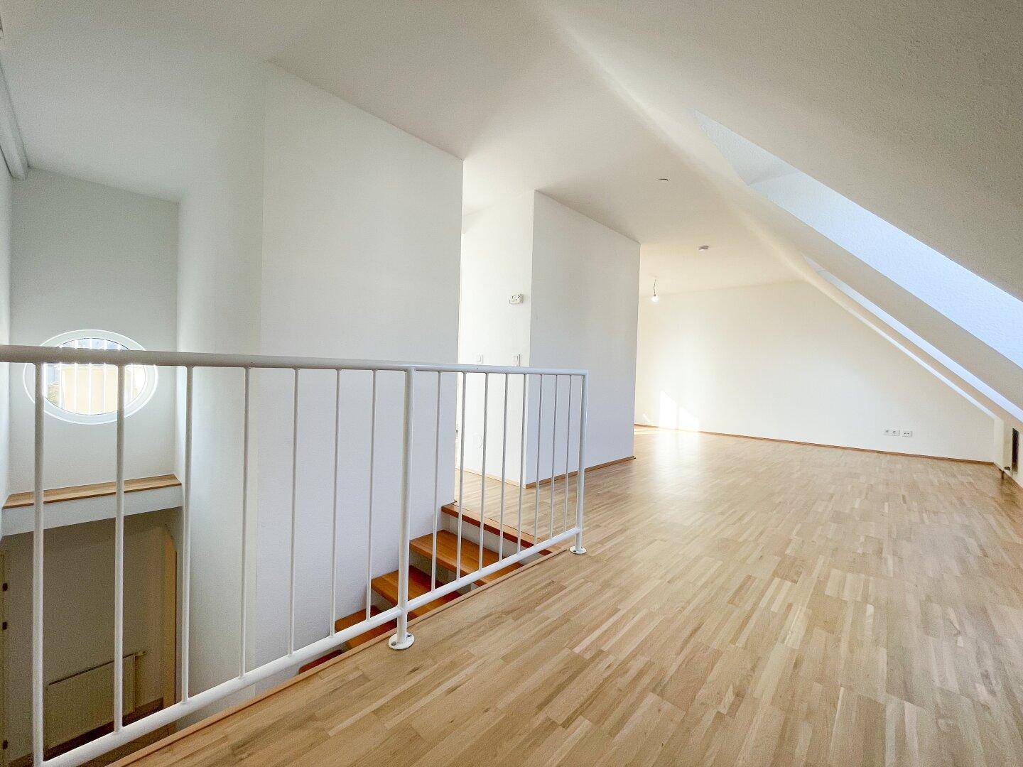 Heller Treppenaufgang im Dachgeschoss mit Holzstufen und weißem Geländer, führt zu weiteren Räumen.