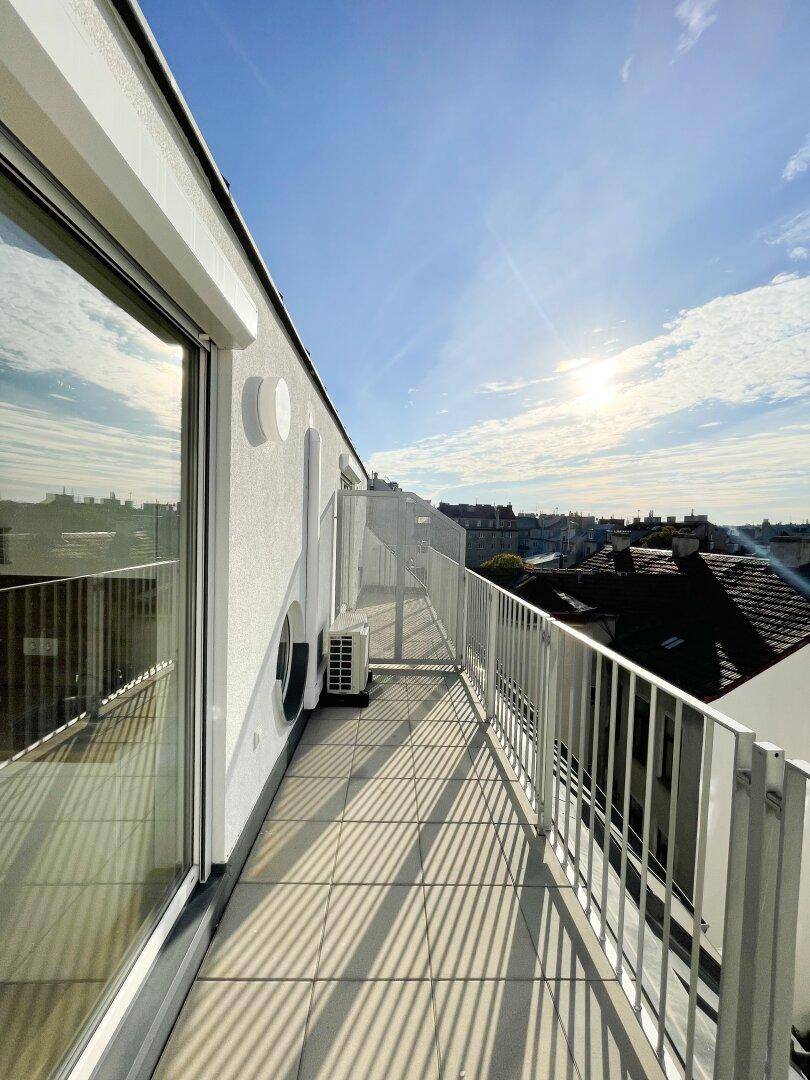 Lange Dachterrasse mit Fliesenboden und Glasfront, bietet einen sonnigen Außenbereich.