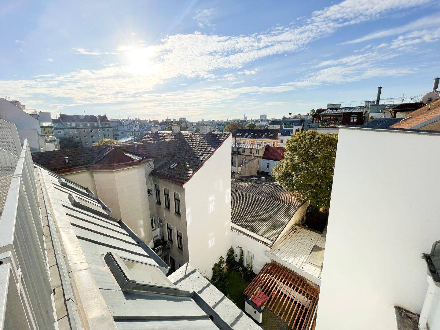 Panoramablick von der Dachterrasse über die Dächer der Stadt und grüne Bäume.