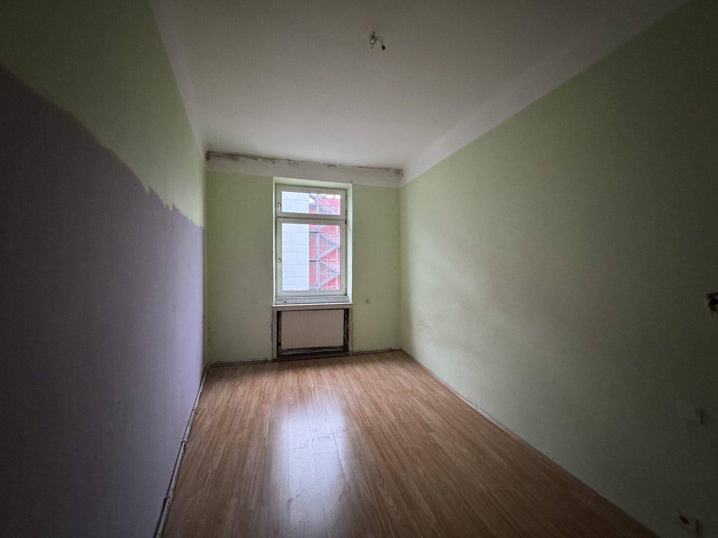 Helles Zimmer mit hellgrünen Wänden und Laminatboden, ideal für individuelle Gestaltung.