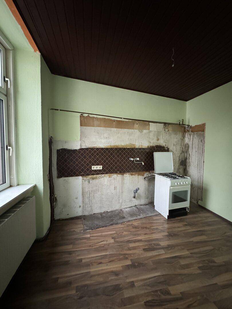 Küche in Renovierungsbedarf mit altem Gasherd und vorbereiteten Anschlüssen für eine neue Einrichtung.