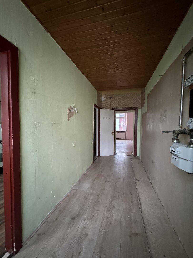 Langer Flur mit Holzbalkendecke und Laminatboden, der zu weiteren Zimmern führt.