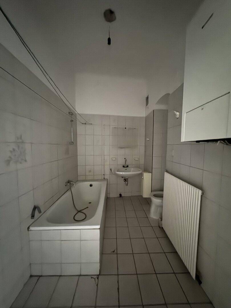 Badezimmer mit Badewanne, WC und Fliesenboden, das eine Modernisierung benötigt.