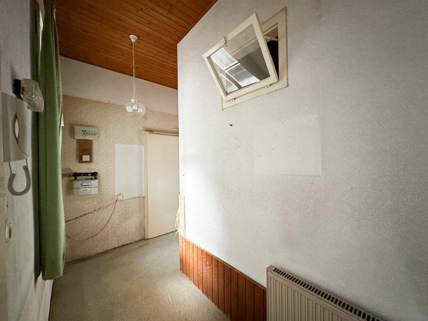 Flur mit Holzdecke, Heizkörper und einem kleinen Oberlichtfenster, das natürliches Licht hereinlässt.
