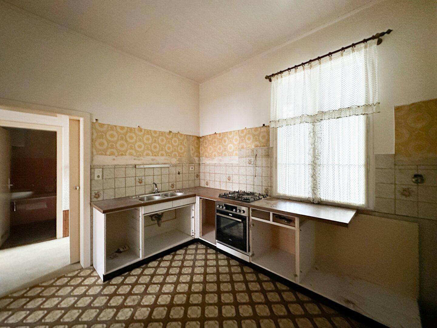 Renovierungsbedürftige Küche mit Gasherd, Spüle und gemusterten Wand- und Bodenfliesen, bereit zur Modernisierung.