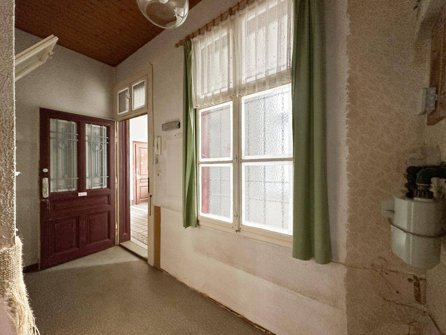Eingangsbereich mit Holztür, Fenster und grünem Vorhang, der auf Renovierung wartet und viel Potenzial bietet.