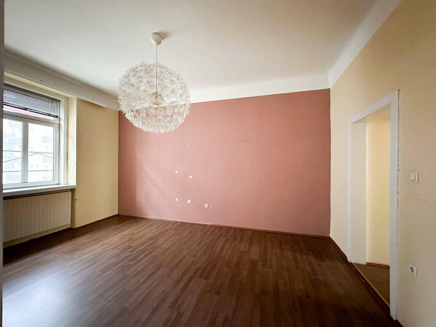 Helles Zimmer mit Laminatboden, farbigen Wänden und einer modernen Deckenleuchte.