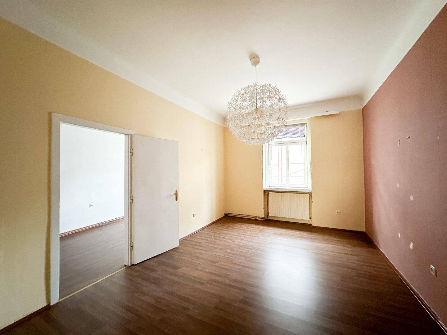 Großes Zimmer mit Laminatboden, farbigen Wänden und Zugang zu einem weiteren Raum.