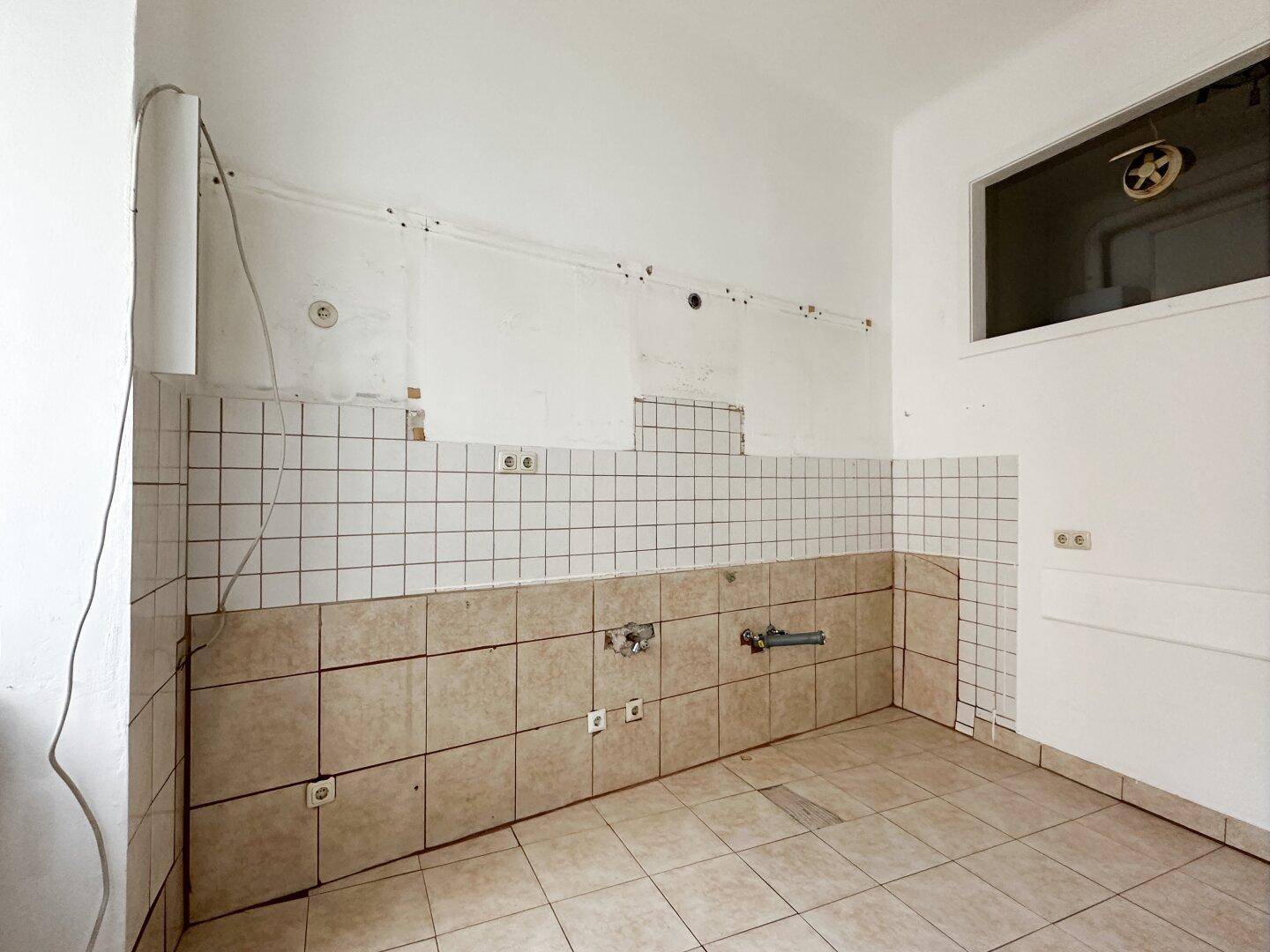 Leerer Küchenraum mit Fliesenboden und vorbereiteten Anschlüssen für eine Einbauküche.