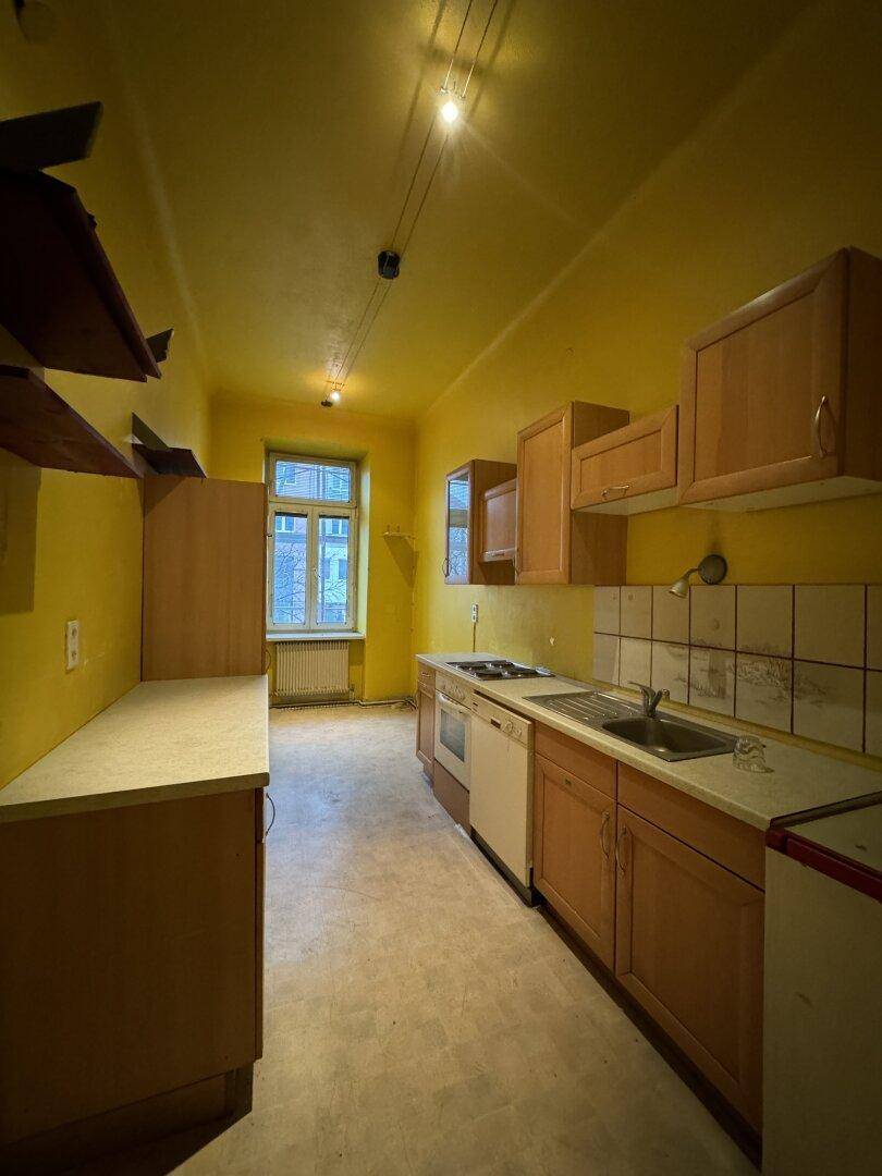 Schmale Küche mit gelben Wänden, einfachen Holzschränken und einer Spüle mit Herd.