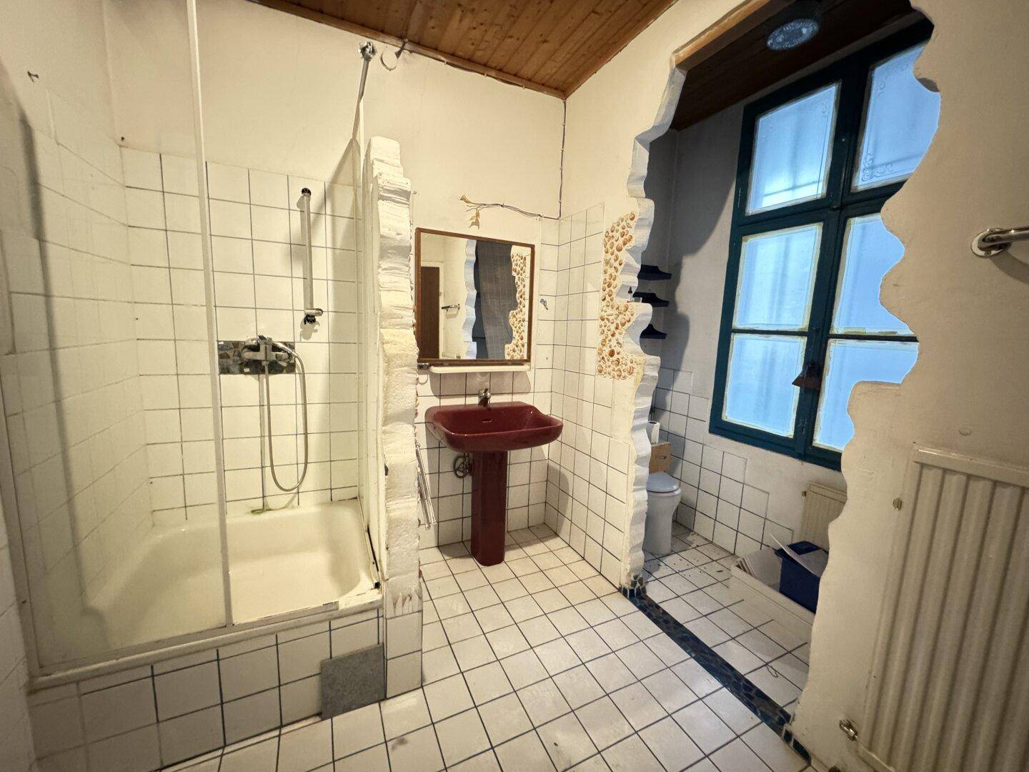 Badezimmer in Renovierung mit weißen Fliesen, einer Duschwanne und einem roten Waschbecken.