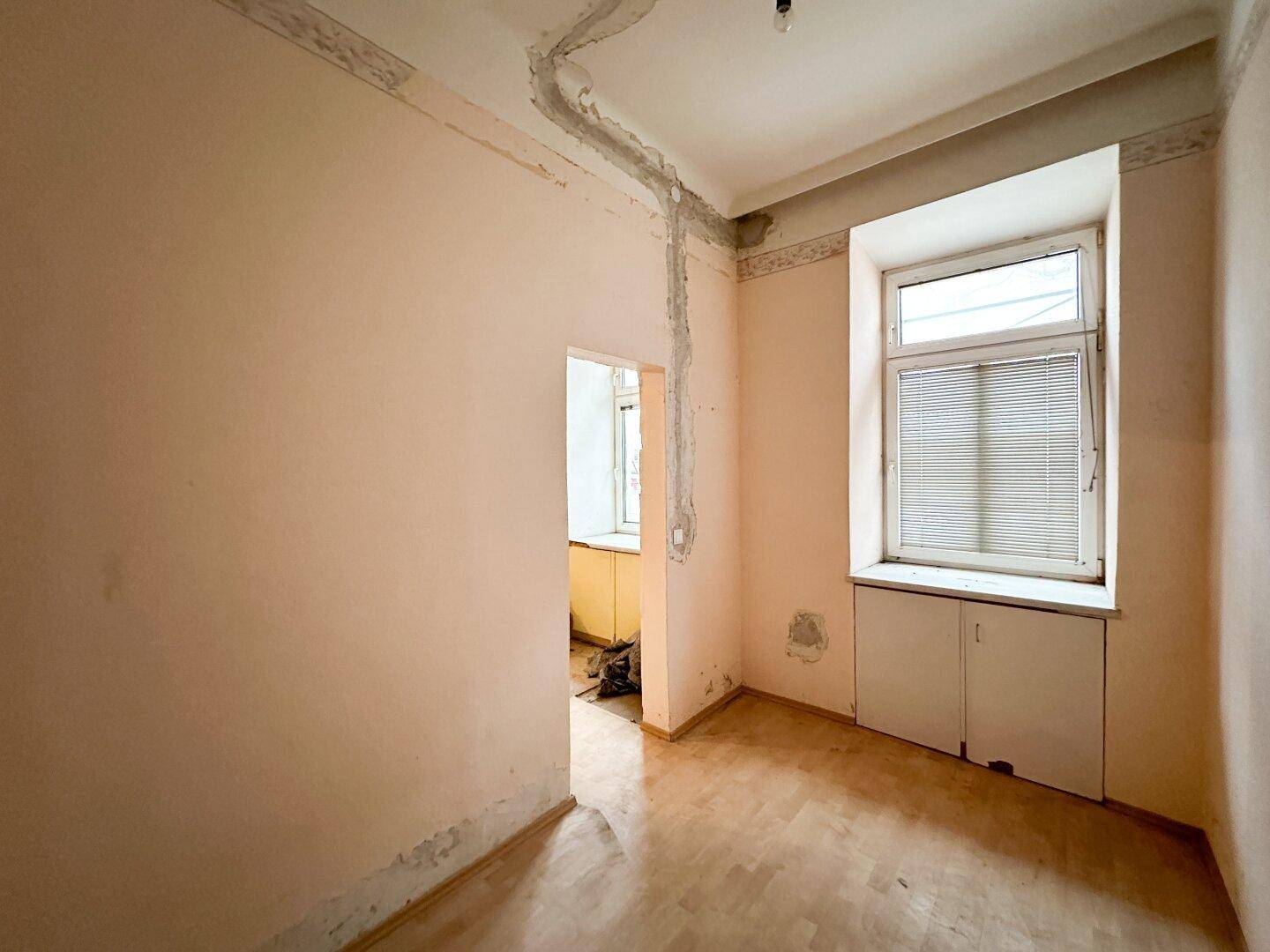 Zimmer mit Parkettboden und Fenster, bereit für die Renovierung.