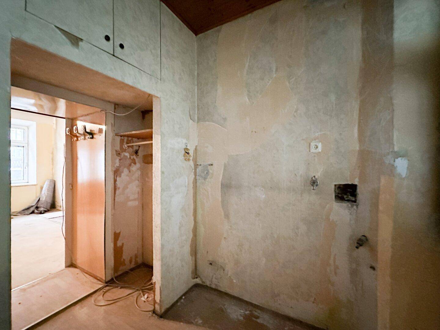 Flur mit Holzbalkendecke und Zugang zu einem weiteren Raum, in Renovierung.