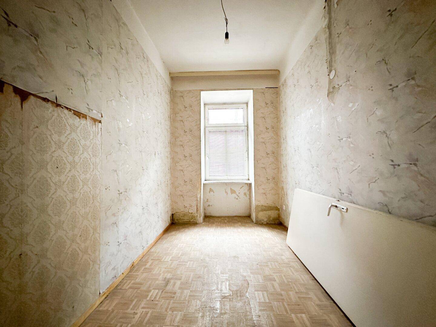 Kleines Zimmer mit Parkettboden und Fenster, bereit für die Sanierung.