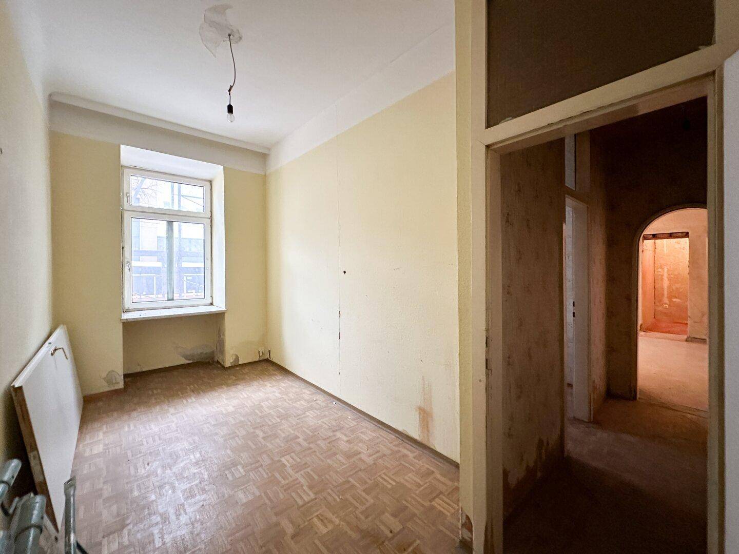 Helles Zimmer mit Parkettboden und Fenster, in Renovierungszustand.