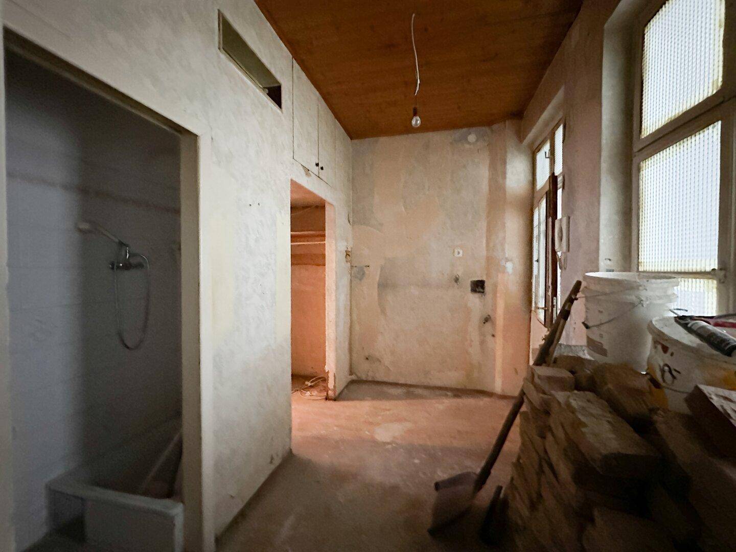 Raum in Renovierung mit Holzbalkendecke und einfacher Duschvorrichtung.