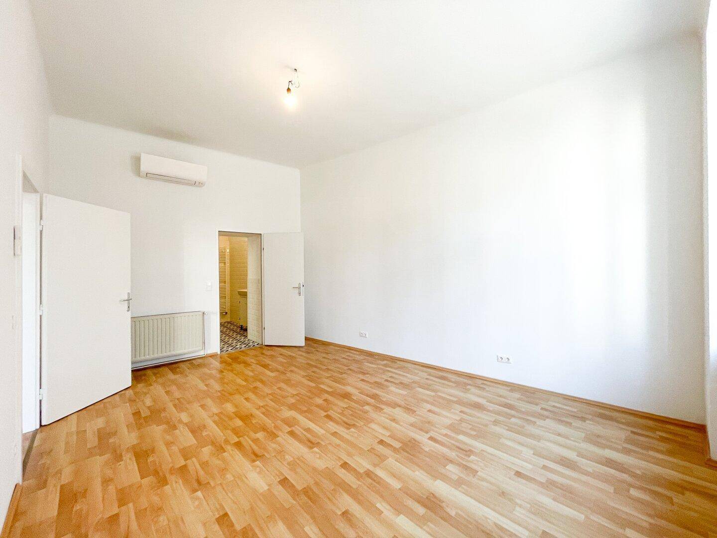 Geräumiges Schlafzimmer mit Parkettboden, Klimaanlage und Zugang zu einem weiteren Raum.