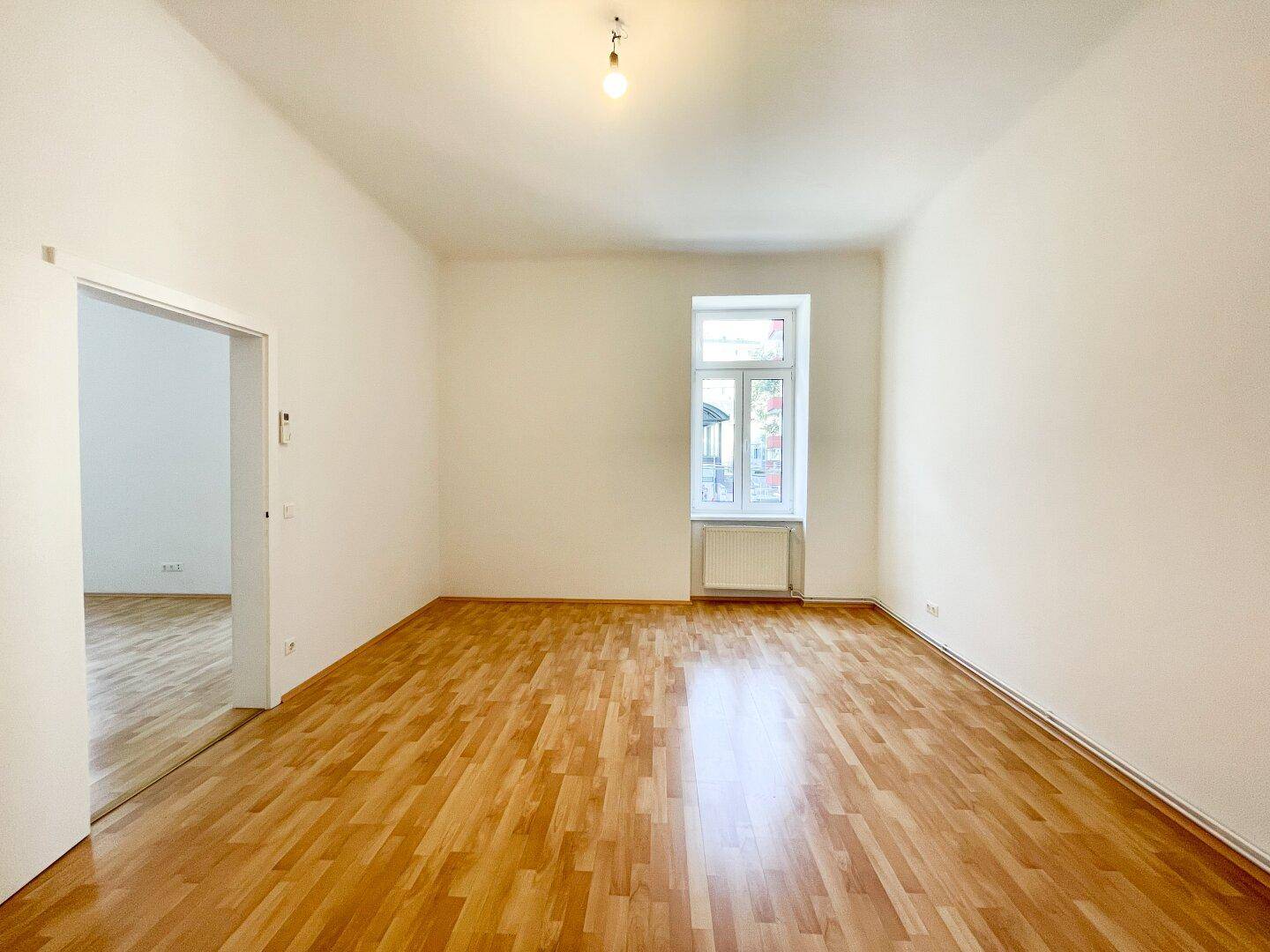 Helles Schlafzimmer mit Parkettboden, weiß gestrichenen Wänden und einem großen Fenster.