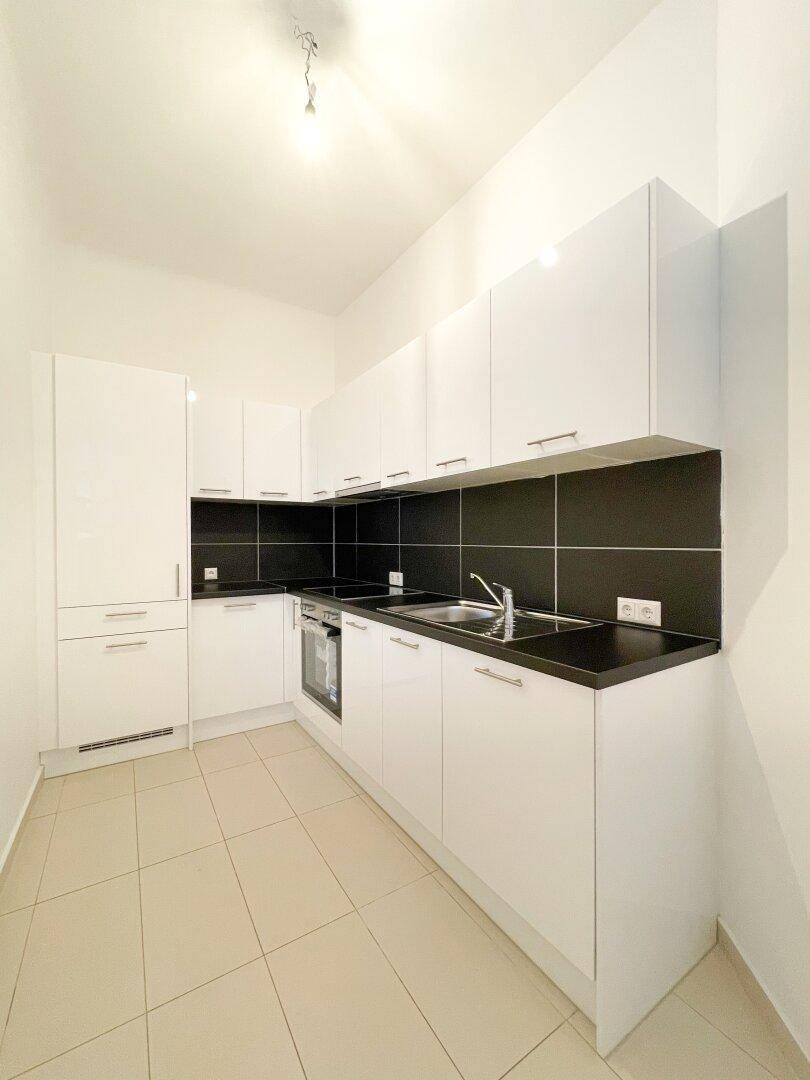 Moderne Einbauküche mit weißen Hochglanzschränken, dunklen Arbeitsplatten und Fliesenboden.