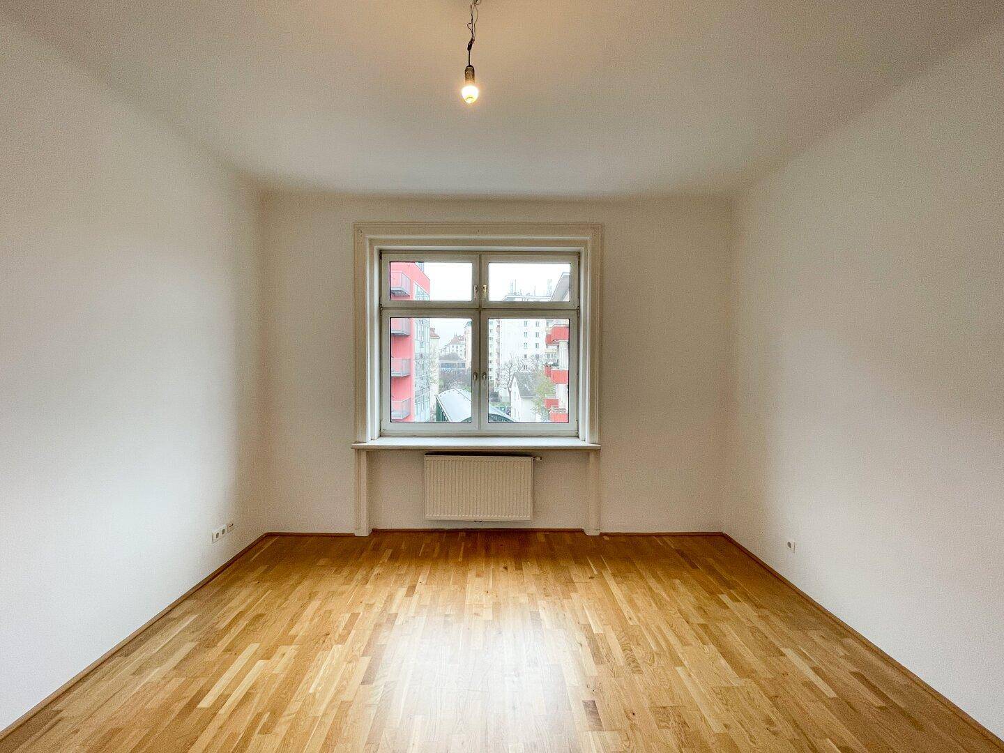 Geräumiges, unmöbliertes Zimmer mit glänzendem Parkettboden und Blick auf die Umgebung.