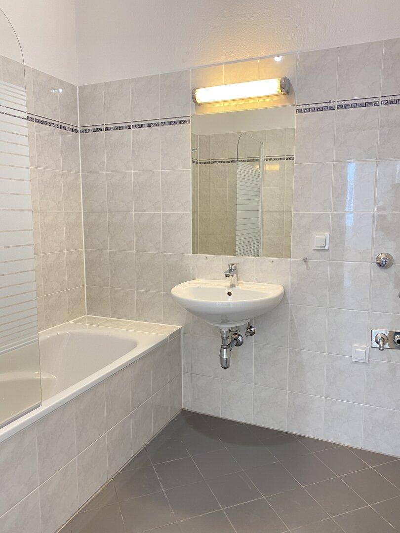 Helles Badezimmer mit Badewanne, Waschbecken und Wandfliesen in neutralen Farben.