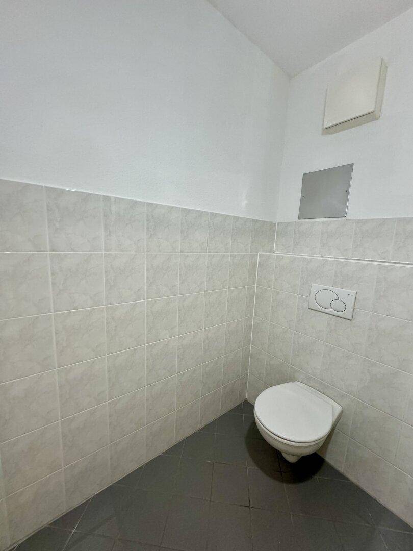 Separates WC mit wandhängender Toilette, hellen Fliesen und dunklem Fliesenboden.