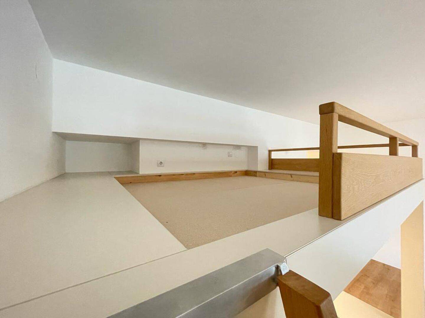 Gemütliche Schlafnische auf der Empore mit Holzgeländer und Teppichboden.